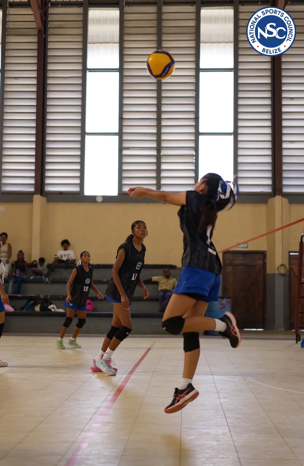 A volleyball player mid-air during a jump serve in a women's match at the NSC Super Nationals